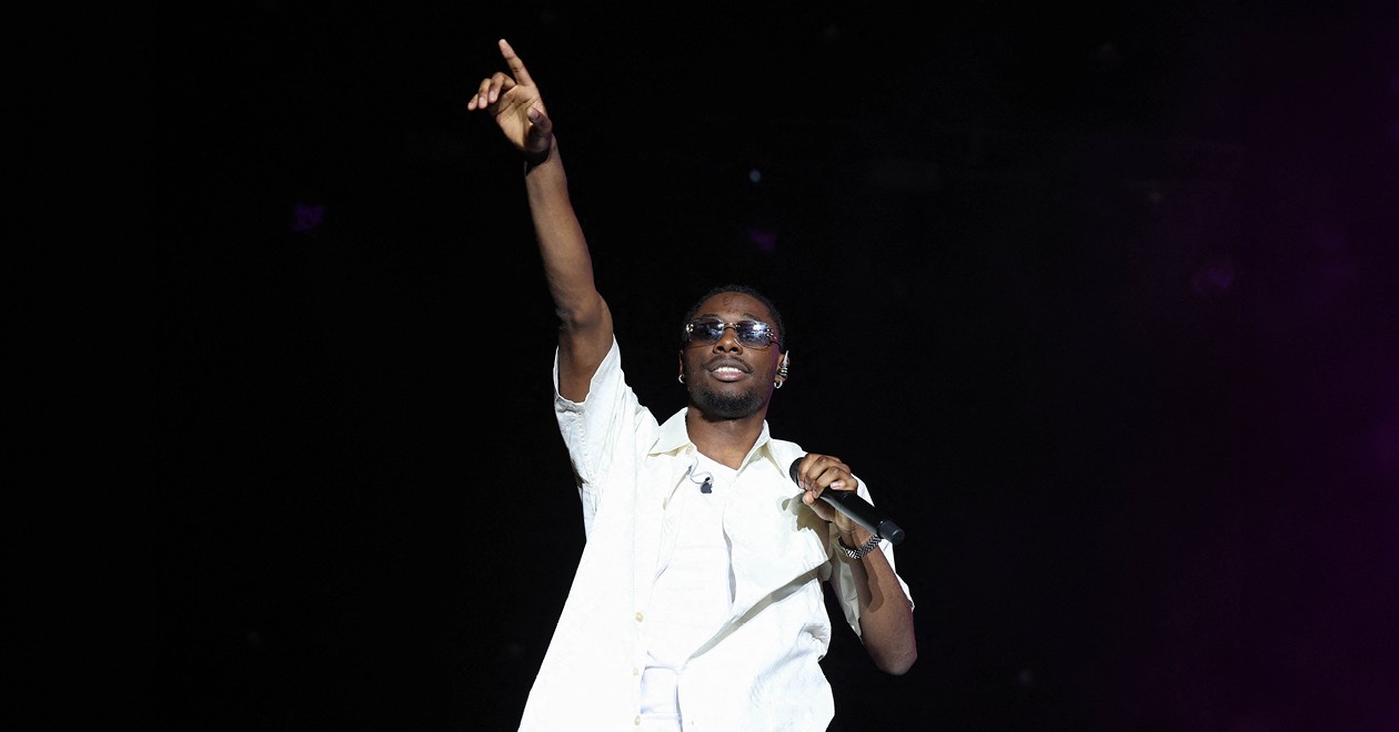 Tiakola performing live, microphone in hand, arm raised toward the audience